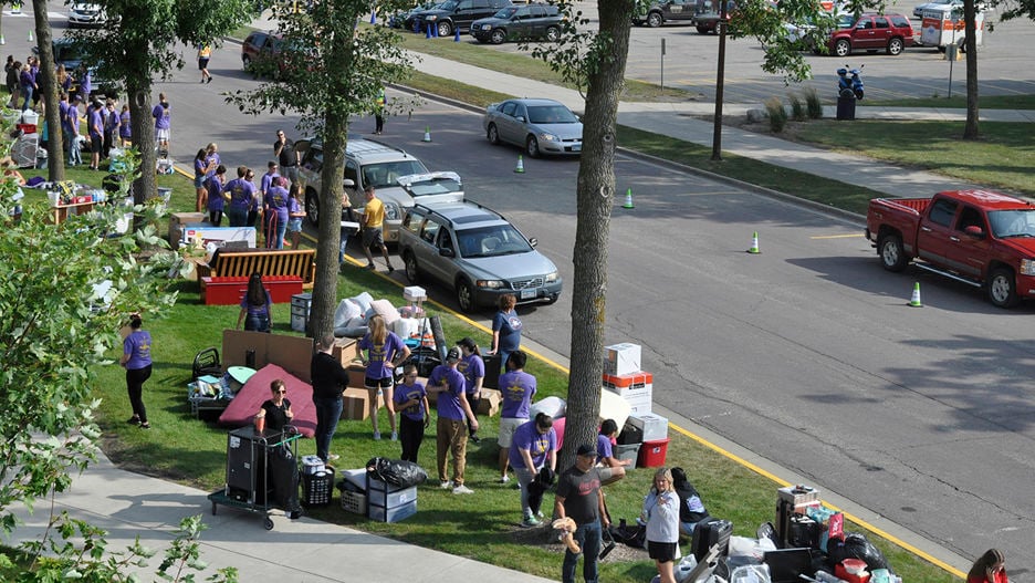 Dorm move in rush, with group of people carrying things from cars to the dorms