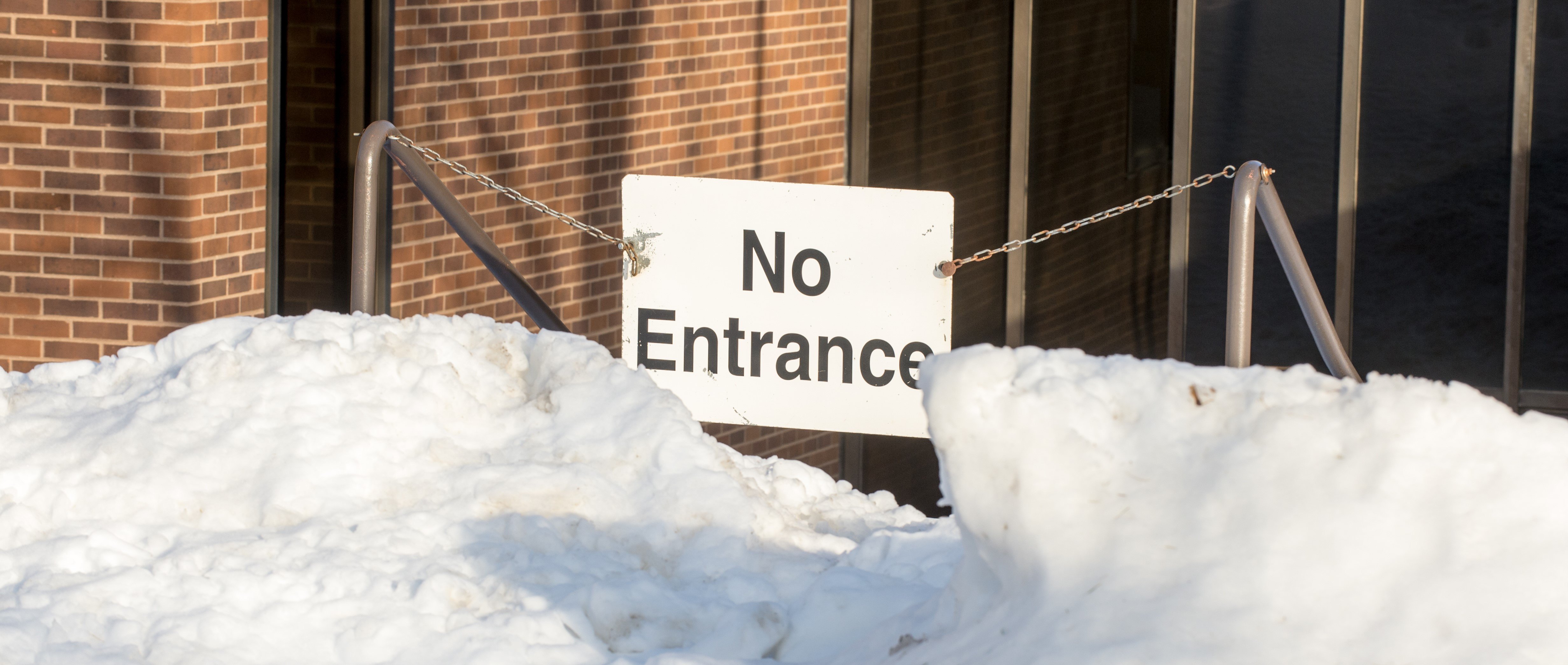 A sign reading No Entrance is chained across the top of an outdoor staircase blocked with snow