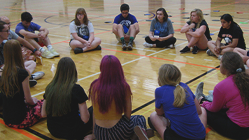 students sitting down in a circle at the gym
