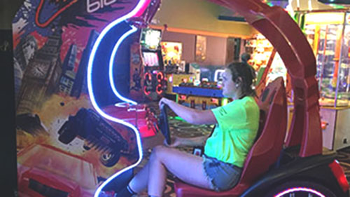 ETS student playing a racing video game at an arcade