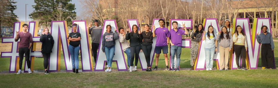 Photo of the Engagement Ambassadors posing outside on campus around the #MavFam sign
