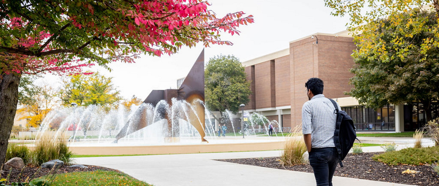 A student walking with a backpack heading toward the fountain on campus