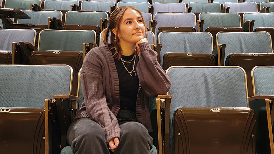 Music industry student Bailey Frerichs sitting in the auditorium with her elbow on the arm rest and her head resting on her hand looking off to the distance