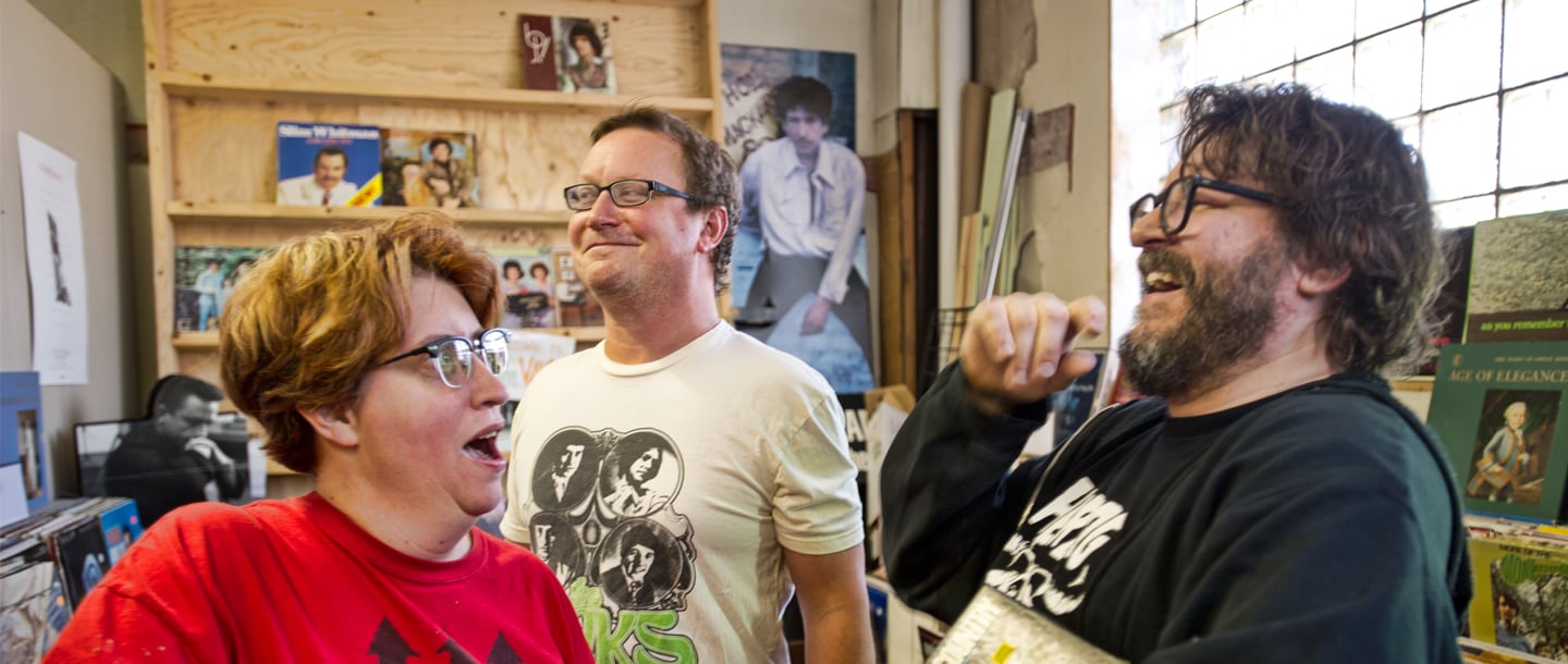 One person making a funny face and two people laughing while looking at record albums
