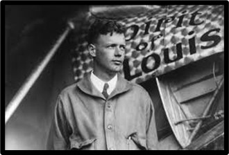 A black and white photo of Charles Lindbergh, an air-mail pilot, standing next to an airplane called the Spirit of St. Louis