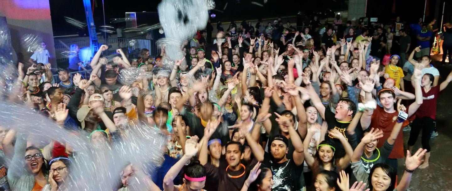Students at a foam party with their hands in the air sticking the maverick sign with their fingers at Minnesota State University Mankato