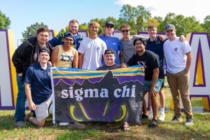 Sigma Chi members posing outside on campus holding the Sigma Chi flag