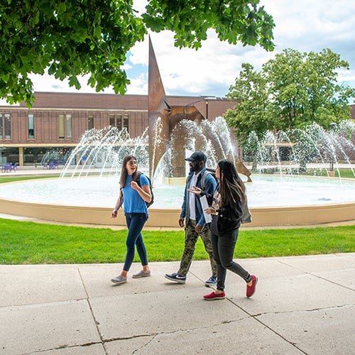 Three students walking by the fountain