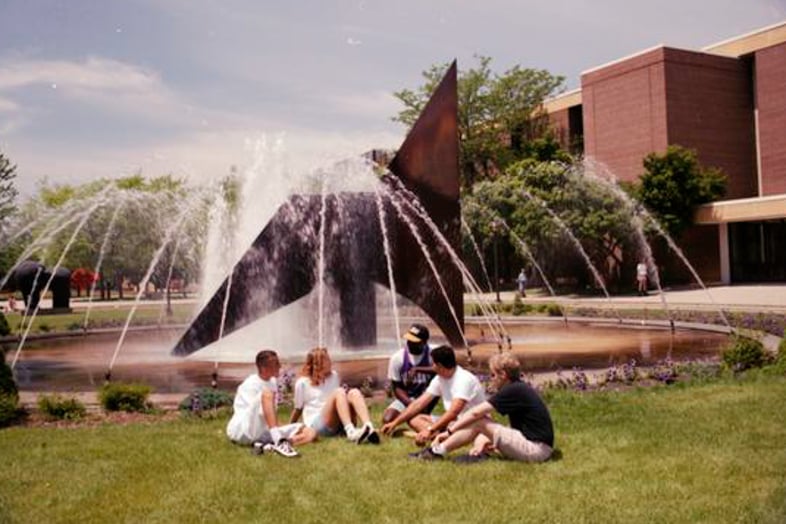 a group of people sitting in the grass under a fountain