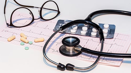 A stethoscope, glasses, few pills, and a printed heartbeat record on a table