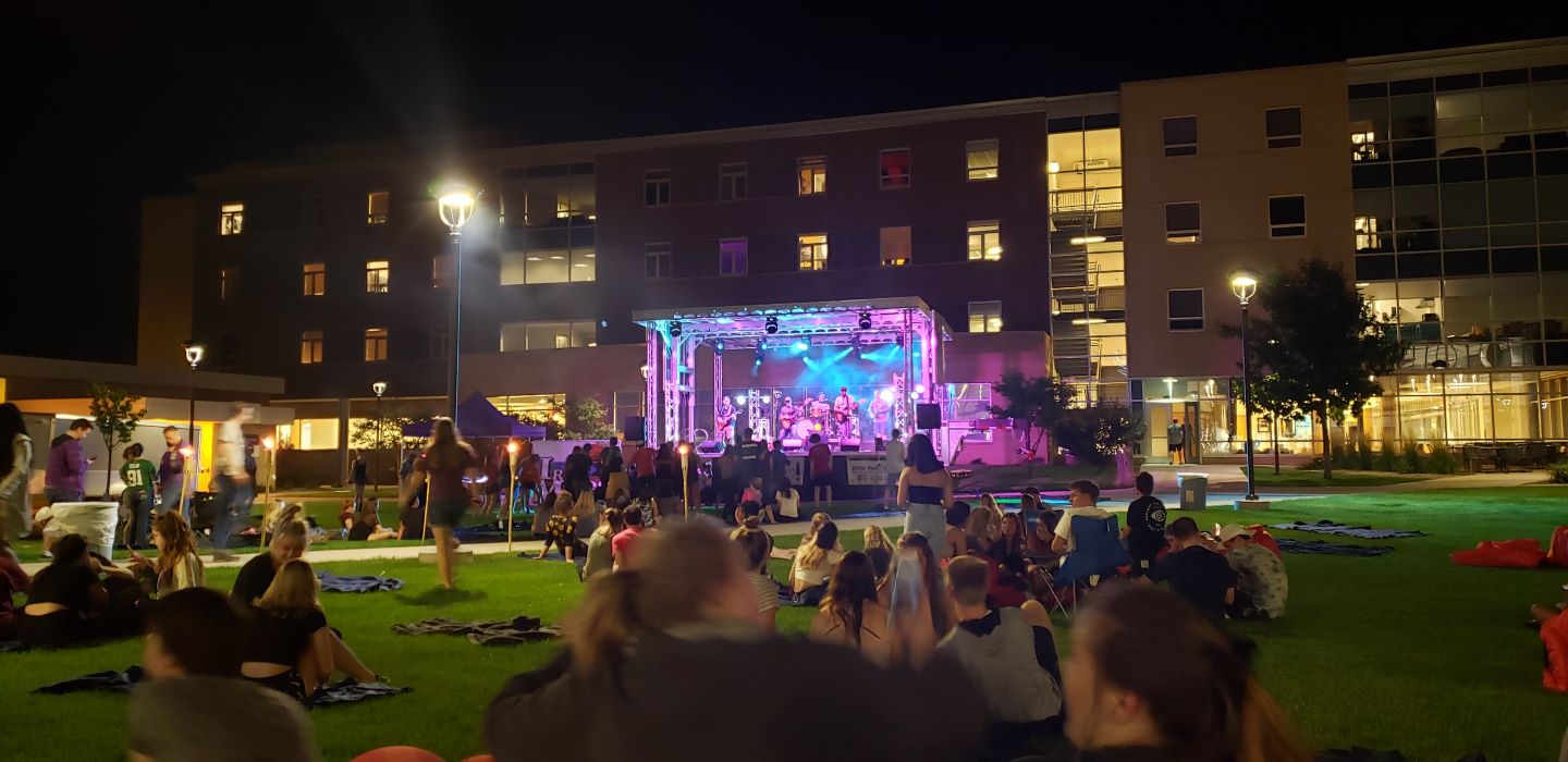 Students, on the lawn in front of a dorm, enjoying live music