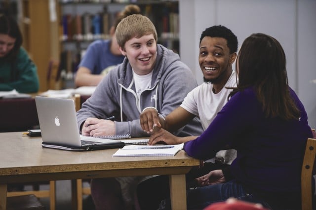 Three students laughing while working together on a macbook