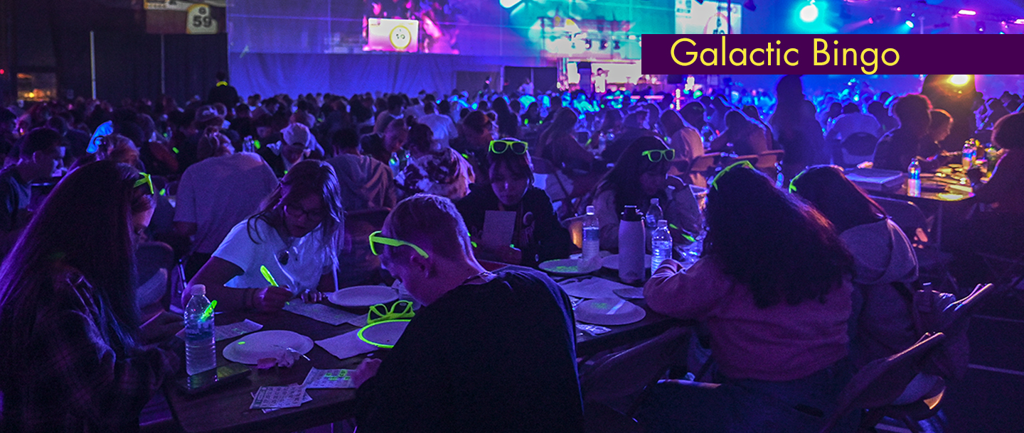 Students sitting at different tables playing bingo using glowing pens and wearing glowing glasses