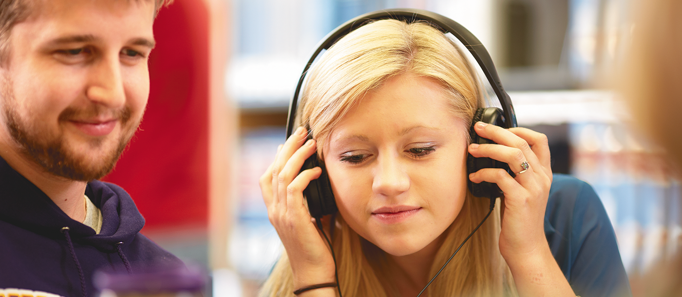 One student listening to headphones while another student smiles