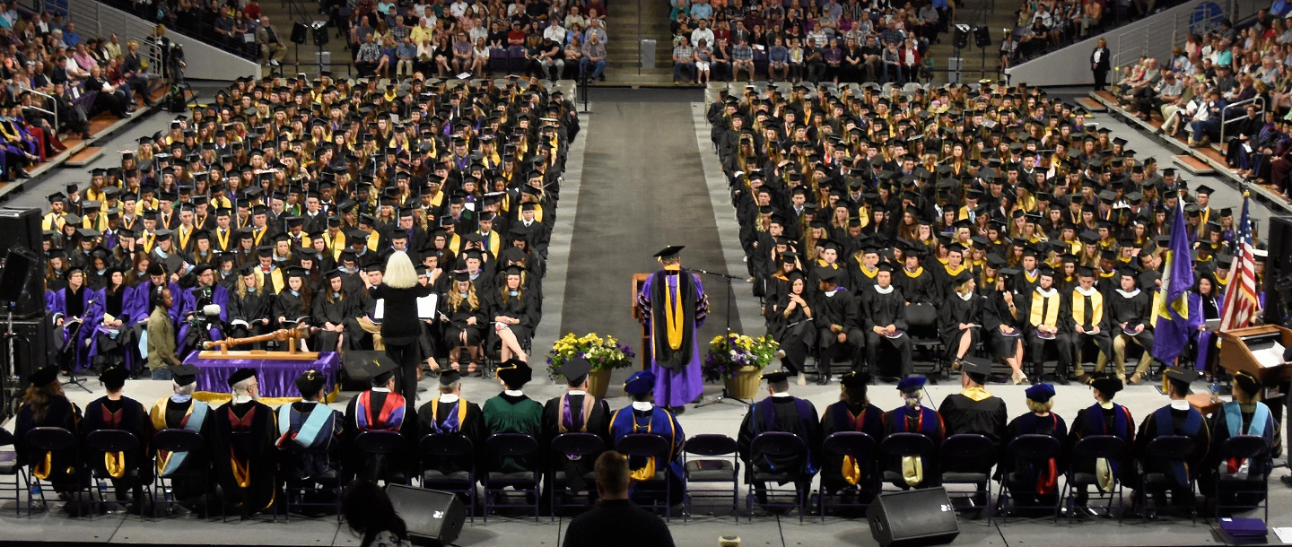 Students sitting down listening to another student giving a speech and looking at an interpretor during their graduation ceremony