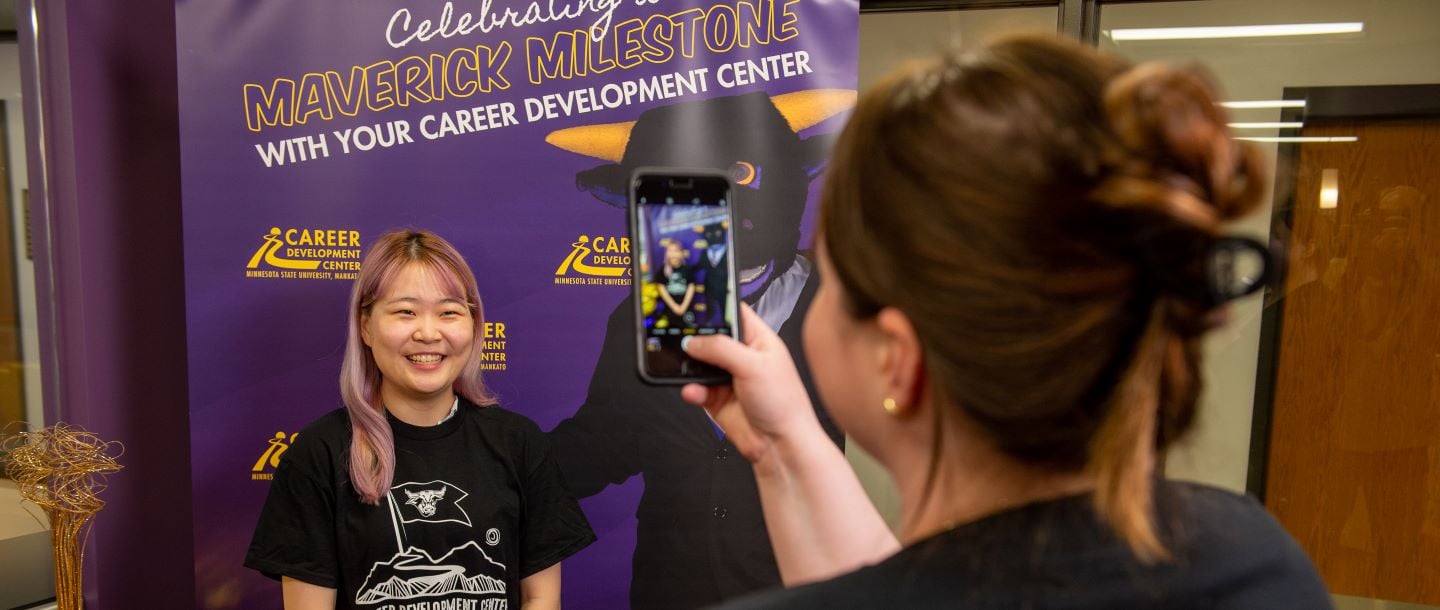 A student getting her picture taken infront of the celebrating a maverick milestone banner at the career development center