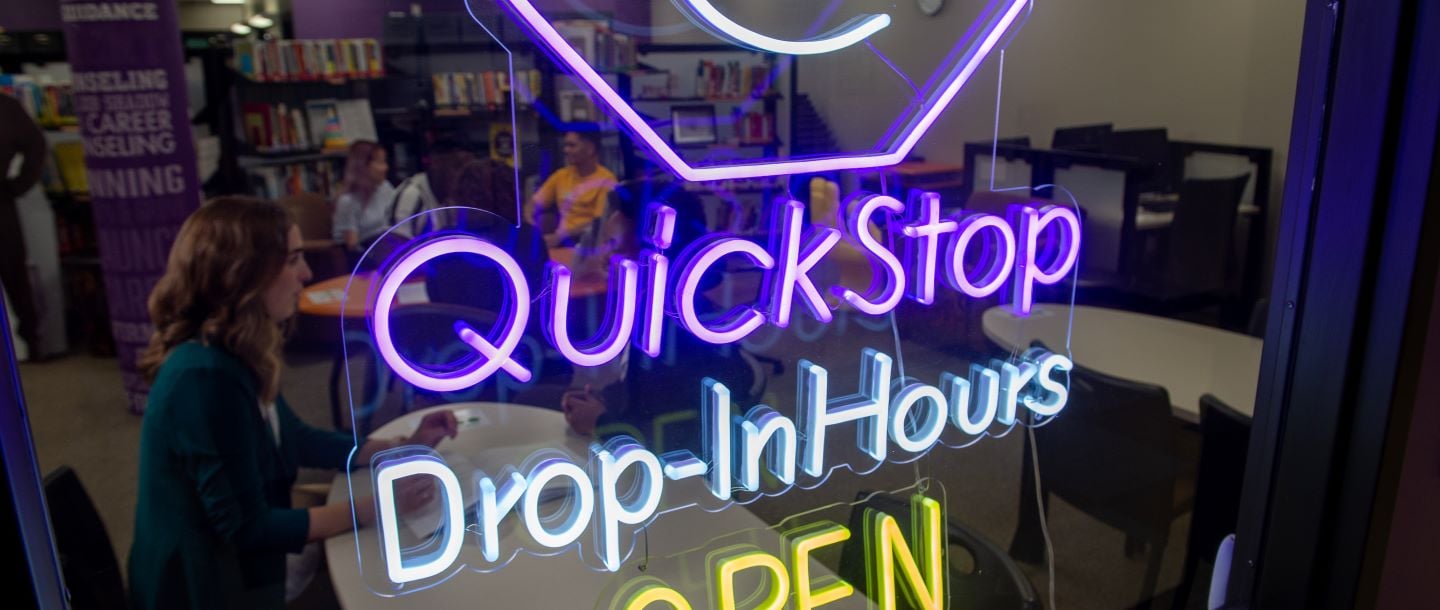 Quick stop drop in hours open neon sign hanging in the window of the career development center