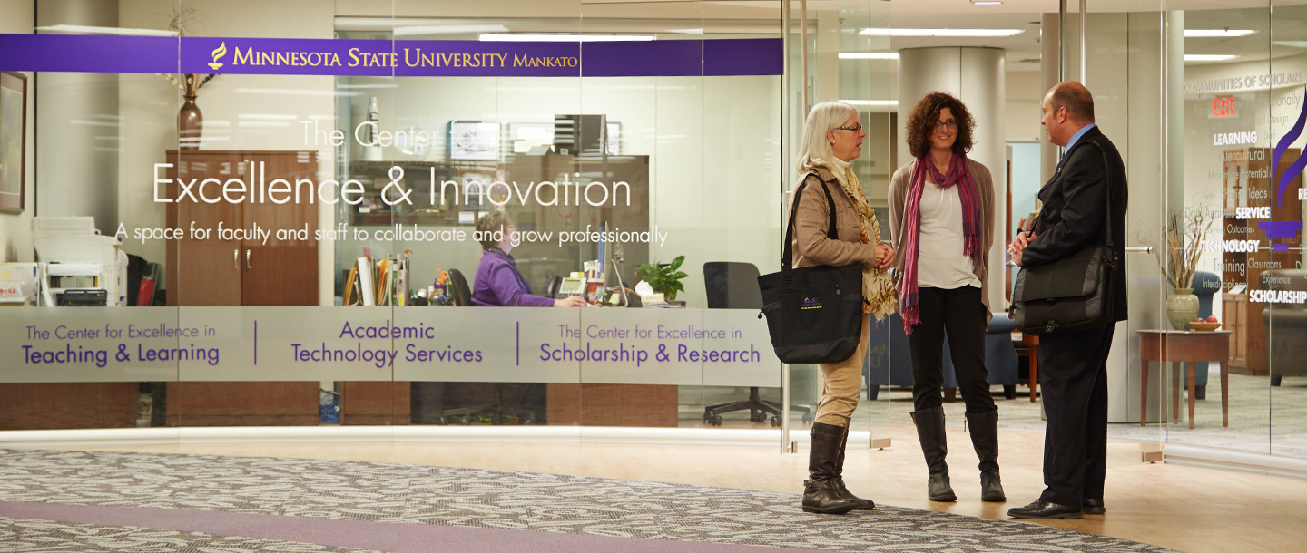 Three faculty members having discussion outside of the Center for Excellence and Innovation office