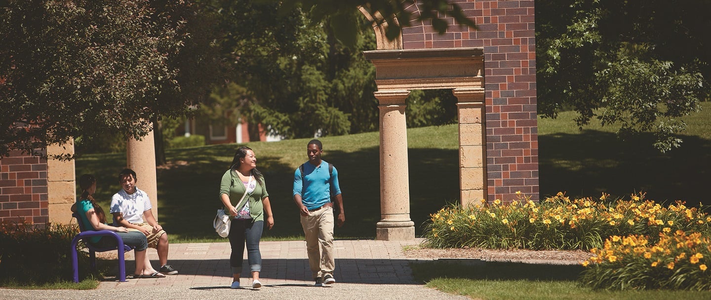 students walking on campus with the arch in the background