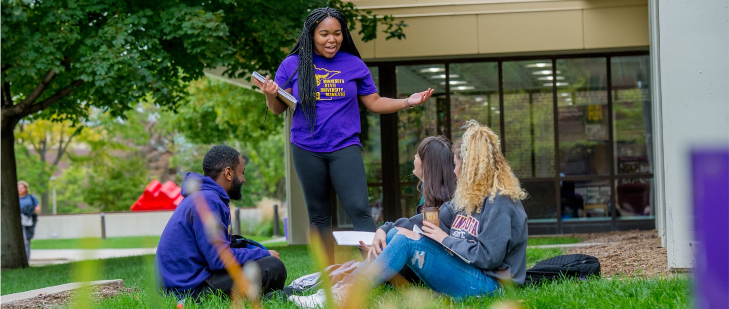 A group of four students in a conversation outside the library