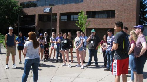 A large group of students listening to the tour guide outside on campus