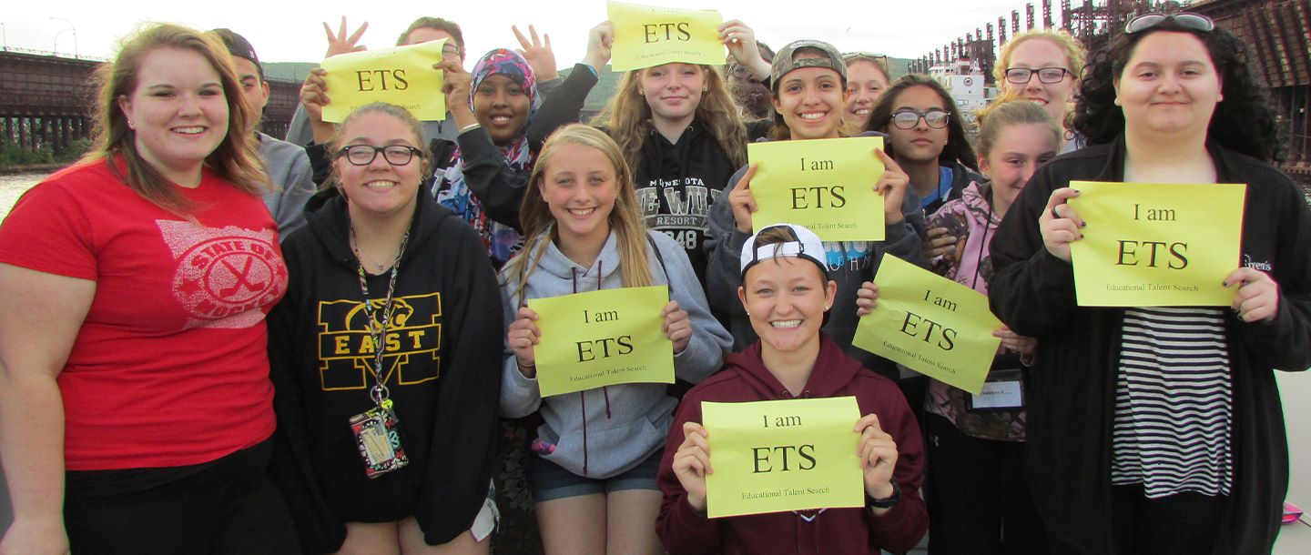 ETS students posing outside with signs that say I am ETS