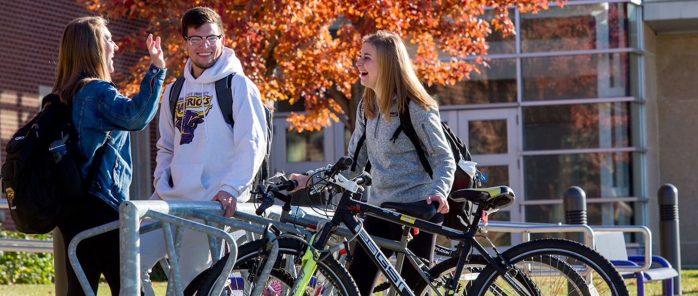 Three students taking and laughing with each other outside on campus at a bicycle rack