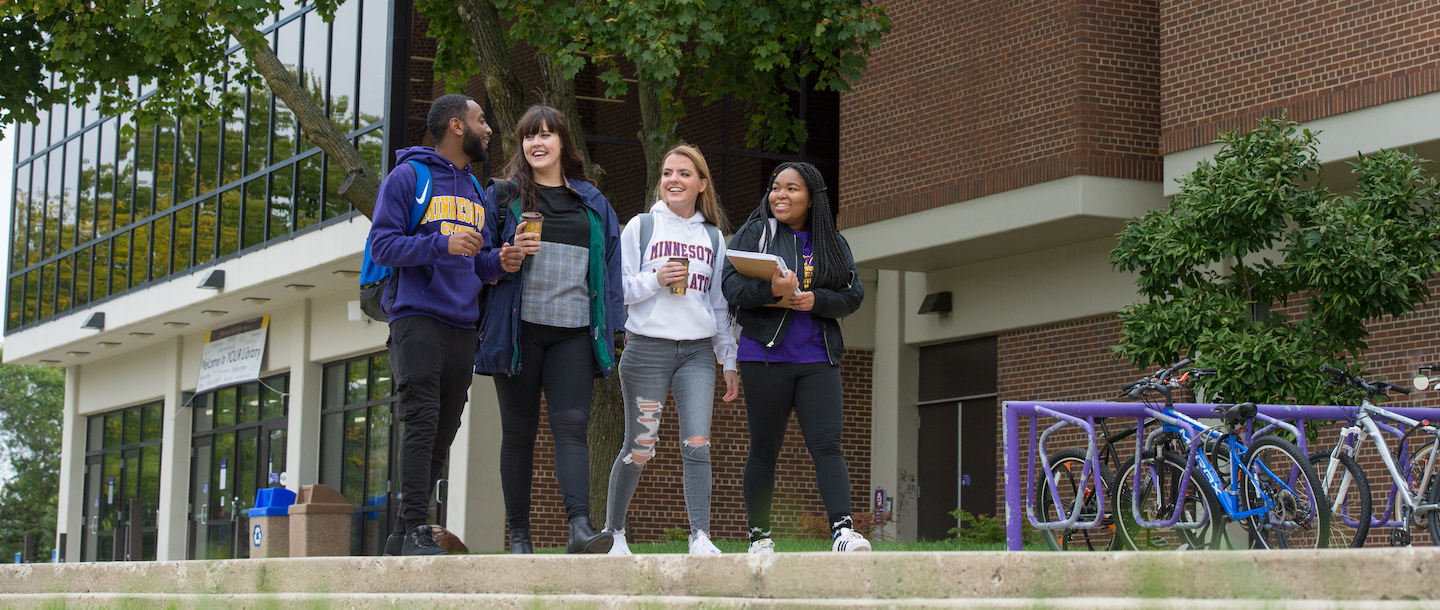 Four students walking and talking with each other in front of the Memorial Library building near the bicycle rack