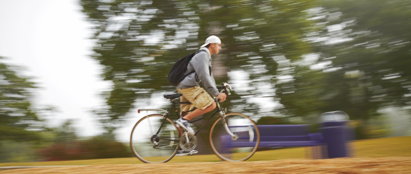A student bicycling on campus near the Bell Tower