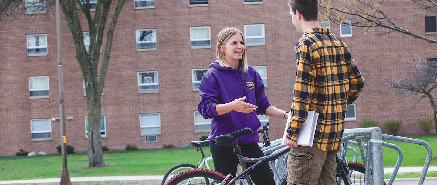 A girl and a guy talking outside on campus at a bicycle rack