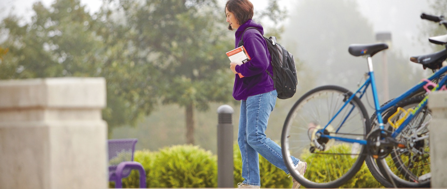 A girl walking by the bicycle stand carrying books