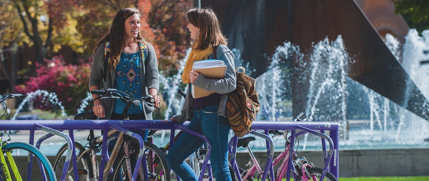 2 girls talking at bicycle rack with the fountain in the background