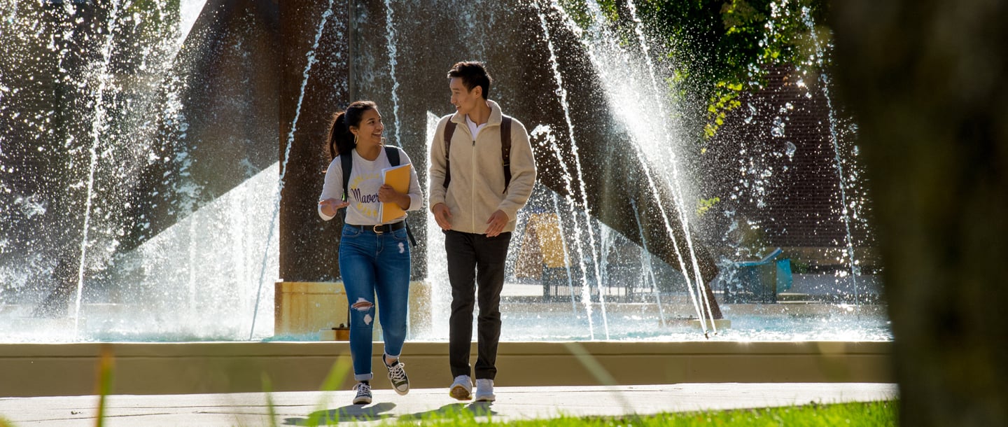 Two international students walking outside on campus by the fountain