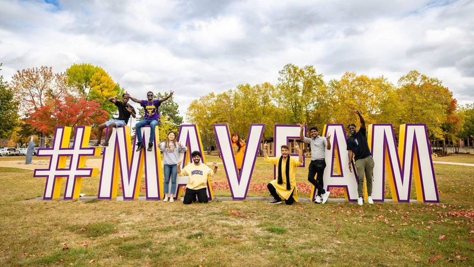 Students posing outside by the big upright letters that spell #MAVFAM