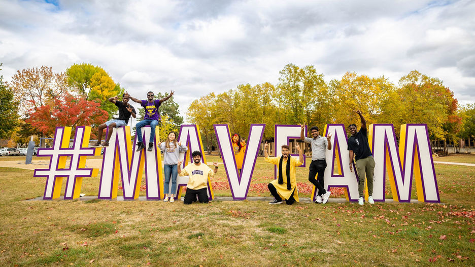 Students posing outside by the big upright letters that spell #MAVFAM