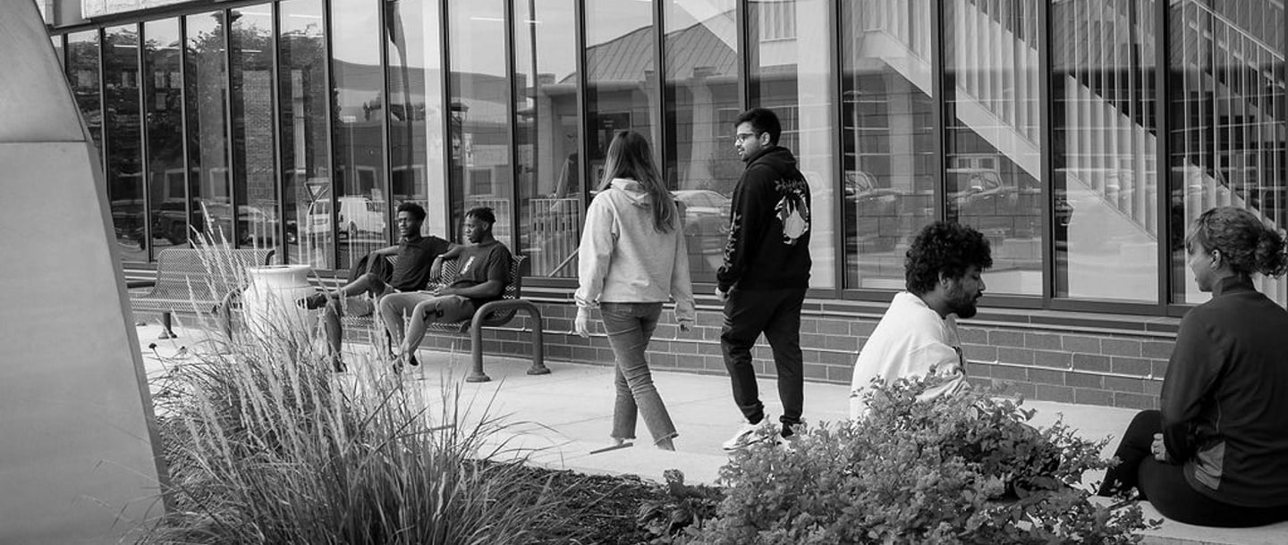 a black and white photo of students sitting and walking in front of the College of Allied Health and Nursing building