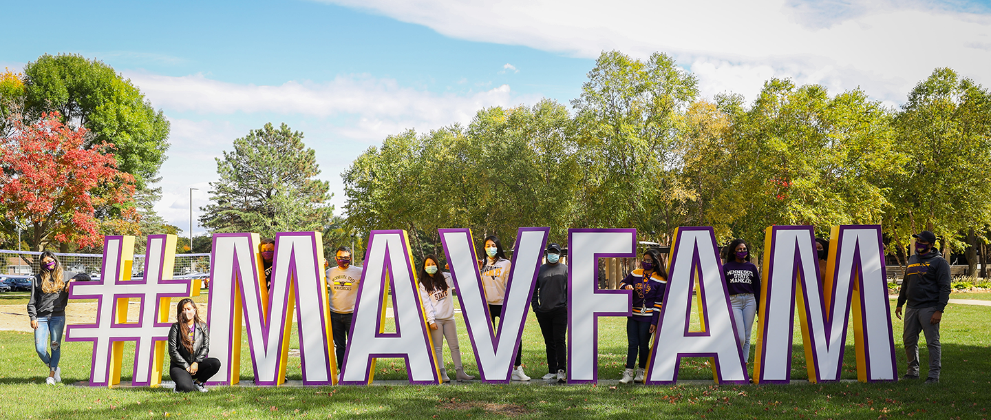 International students standing outside next to letter props spelling hashtag mavfam