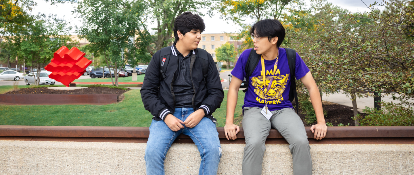 Two students sitting outside on the ledge above the tunnel that connects the Continental Student Union building to Memorial Library