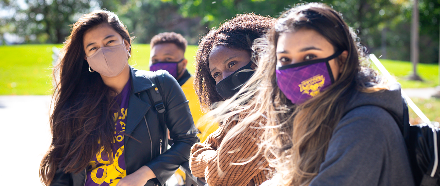 Students wearing masks sitting outdoors on a bench