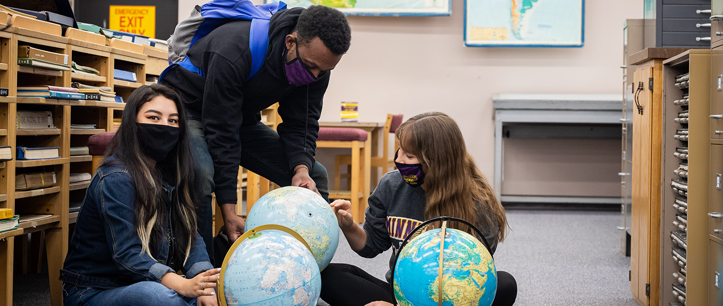 Three students looking at globes in Memorial Library