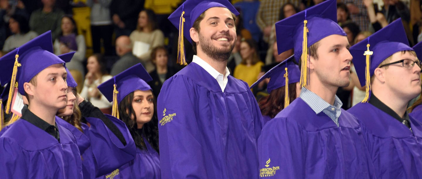 Closeup on some graduates in purple graduation gowns and hats standing at the commencement ceremony with a smile one their face