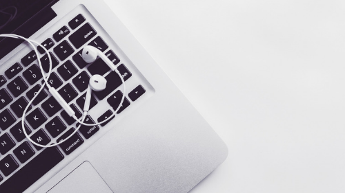 A laptop on a desk with ear buds