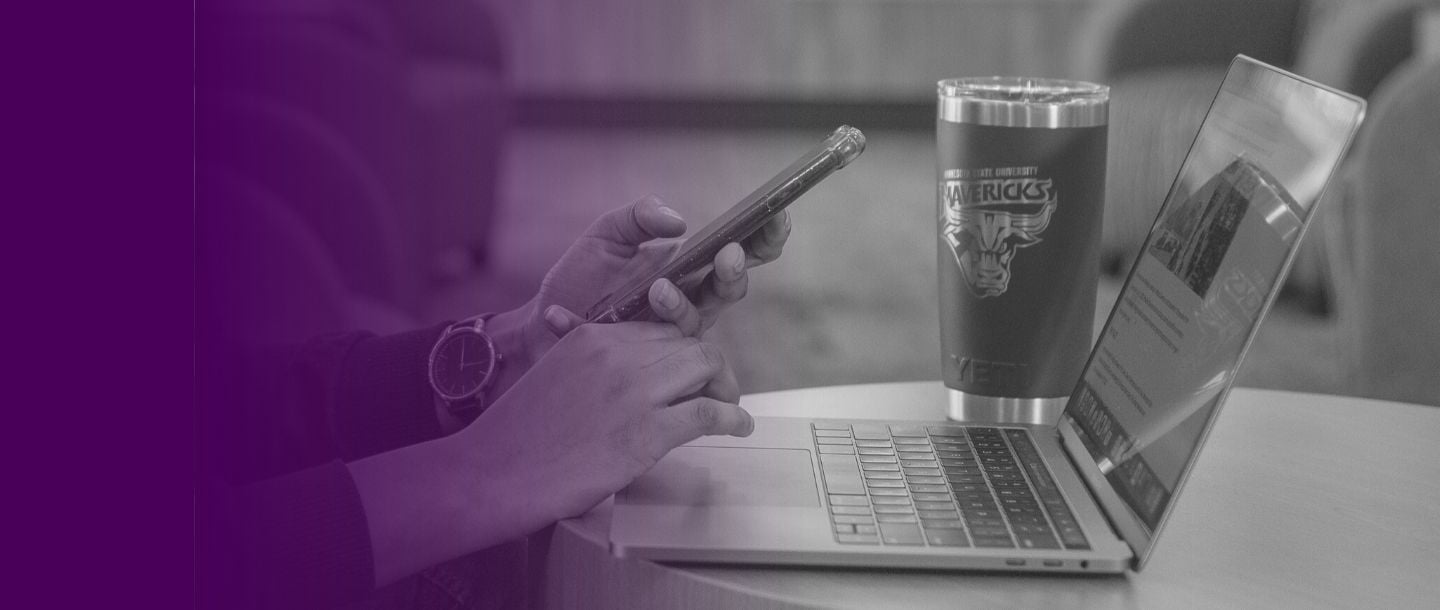 Grayscale image of person holding smart phone and using laptop. Purple gradient effect.