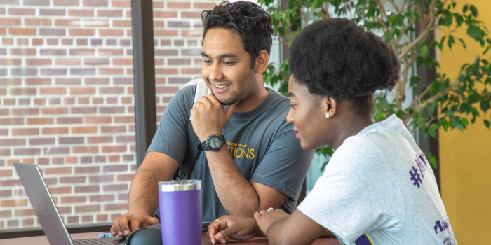 Two students on campus in Memorial Library. Looking at the laptop.