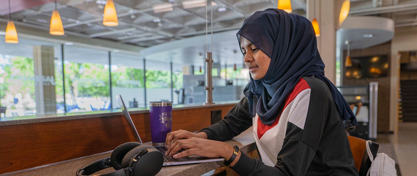 Girl sitting at high table in Jazzman's working on a laptop with a coffee mug and headphones on the table