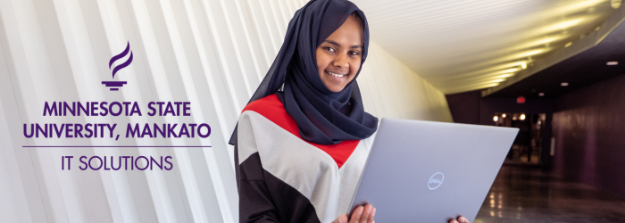 Student smiling at the camera and holding a laptop. In the corner of the photo is the IT Solutions logo.