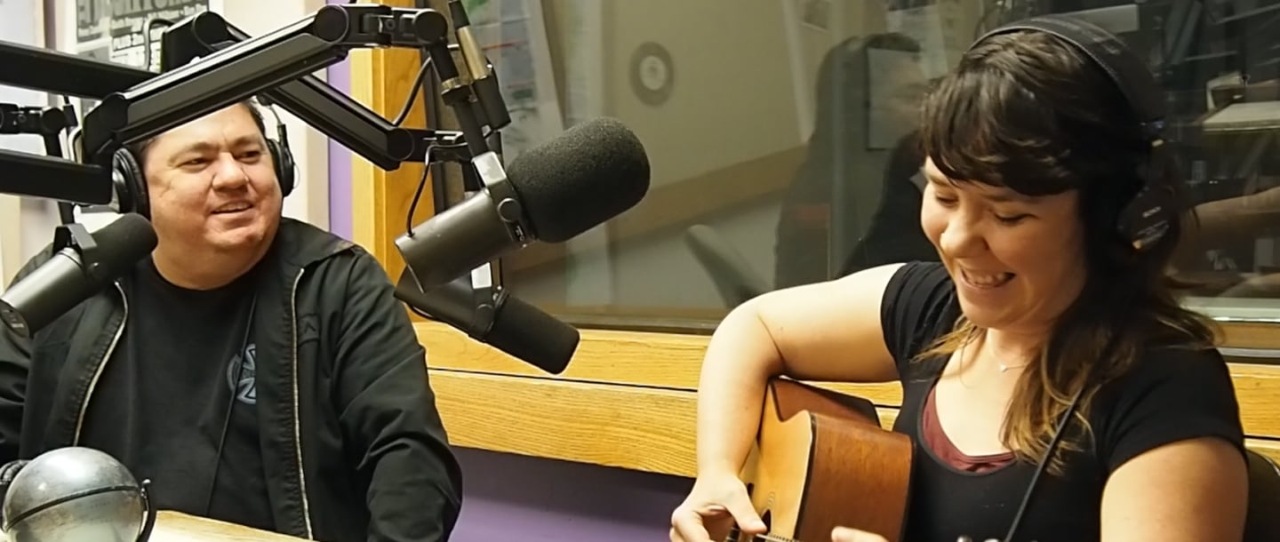 Chuck Rodriguez with a person smiling and playing the guitar inside the KMSU Radio station studio