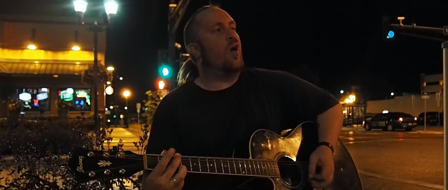"Punk Rock" Tom Heffernan playing a guitar and singing on a sidewalk at night