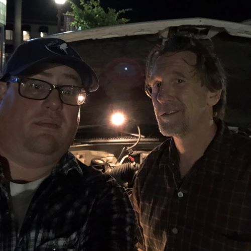 Eric "E Lars" Larson and Eric "E Man" Hendrickson posing outside by the sidewalk at night with a vehicle with the hood up in the background