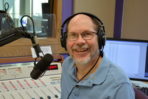 Host of 'Best of Broadway' smiling wearing a headphone with a microphone in front of them